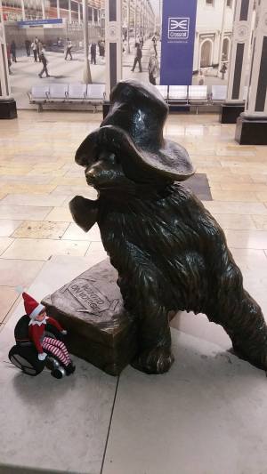 Toy Elf in wheelchair next to a statue of Paddington Bear.