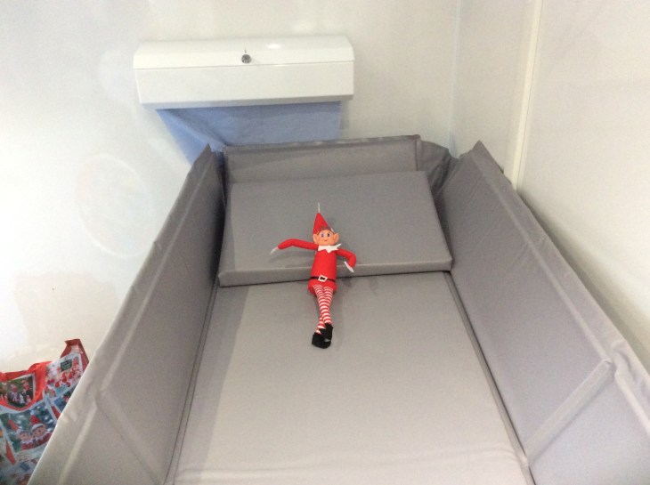 Alfie the Elf is lying on the changing table. His legs are crossed and he is smiling.
